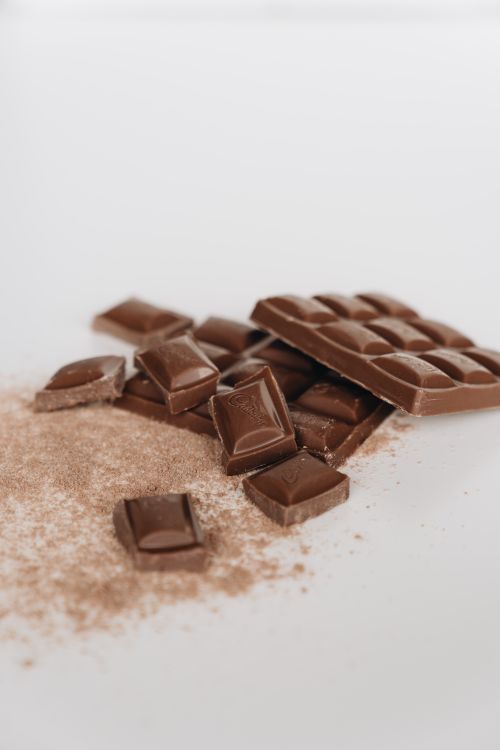 Free A close-up of a chocolate bar with chocolate pieces and cocoa powder on a white background. Stock Photo