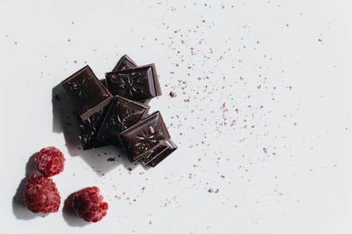 Free Minimalist flat lay of dark chocolate pieces and raspberries on a white background. Stock Photo
