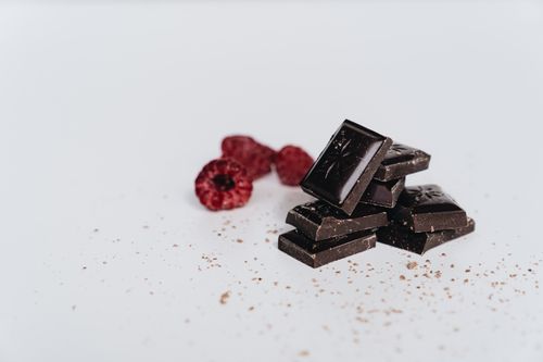 Free Artistic shot of dark chocolate pieces and fresh raspberries on a white backdrop. Stock Photo