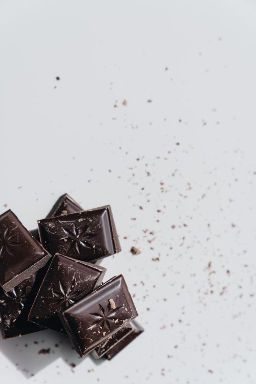 Free Artistic shot of dark chocolate pieces with scattered crumbs on a light background. Stock Photo