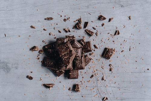 Free Top-down view of broken dark chocolate bars with shavings on a gray background, ideal for food photography. Stock Photo