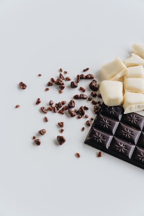 Free Close-up of dark and white chocolate pieces with scattered cocoa nibs on a white background, showcasing texture and indulgence. Stock Photo