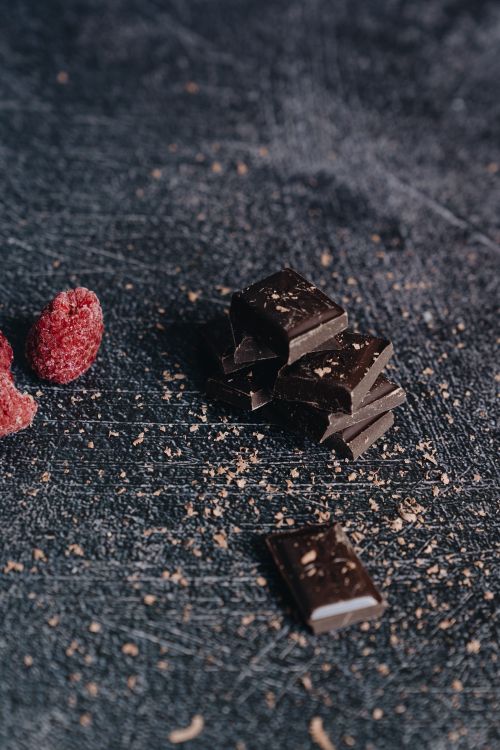 Free Vertical shot of dark chocolate pieces and raspberries on a textured surface, with cocoa dust. Stock Photo