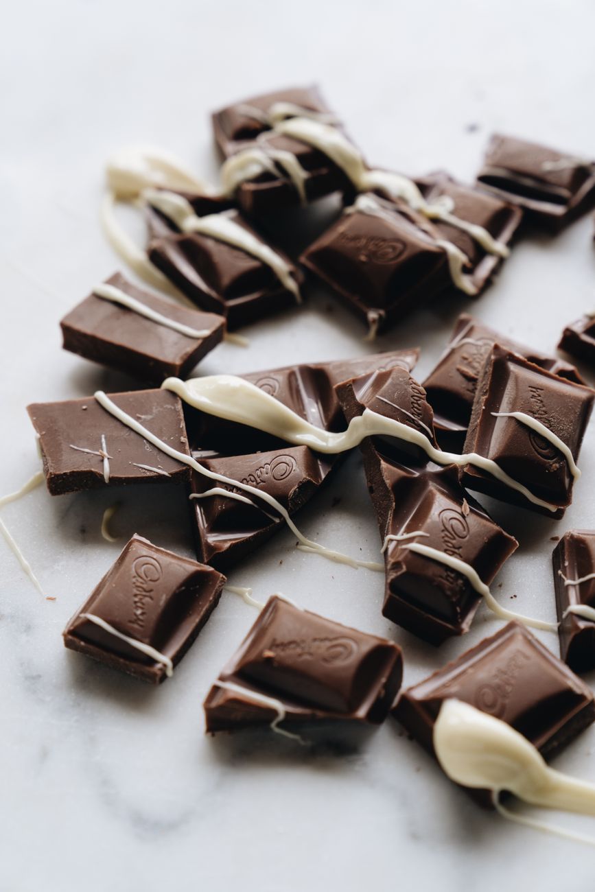 Heerlijke melkchocolade blokjes met artistieke witte chocoladesaus op een marmeren oppervlakte.