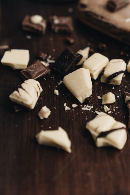 Squares of pale ivory white chocolate broken apart on a dark wood board, showing the smooth, waxy texture inside.