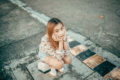 Free Stylish young woman crouching outdoors looking up with thoughtful expression. Stock Photo