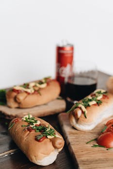 Close-up of appetizing hot dogs garnished with herbs and a can of soda.