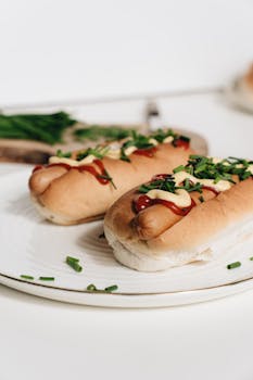Close-up of hot dogs with ketchup and mustard garnished with chives on a white plate.