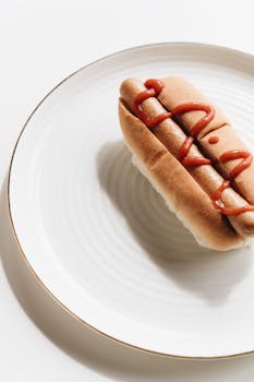 Appetizing hotdog with ketchup on a white plate, perfect for a snack or meal inspiration.