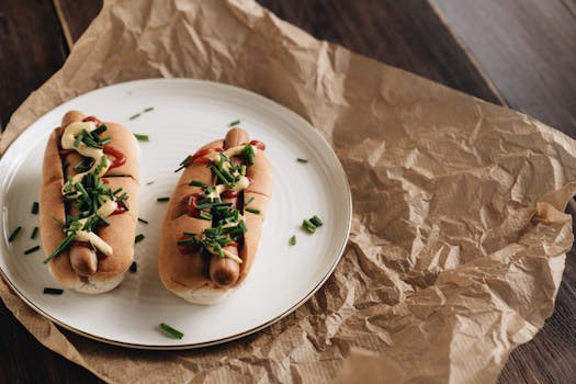 Two hot dogs with mustard, ketchup, and chives on a plate, perfect for quick meals.