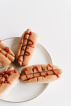 Close-up of hotdogs with ketchup drizzled on a white plate. Perfect tasty snack.