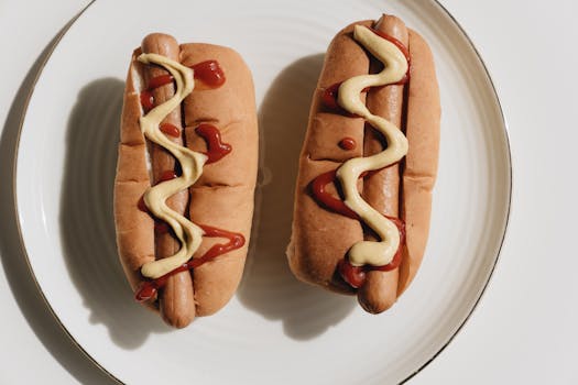 Two hot dogs on a plate topped with ketchup and mustard, ready to eat.