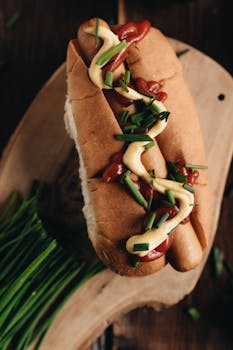 A delicious gourmet hot dog with mustard, ketchup, and green onions on a wooden board.