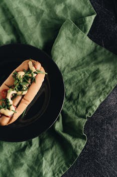 Delicious hot dog with mustard and fresh chives on a ceramic plate, perfect for street food lovers.