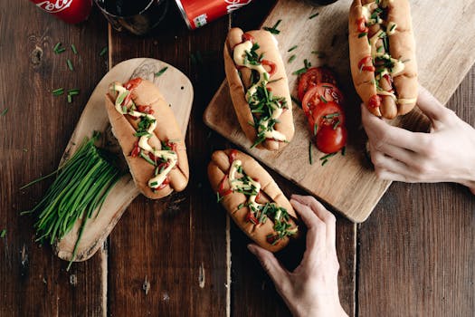 Delicious hot dogs topped with fresh chives and tomatoes on a rustic wooden board.