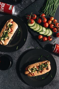 Gourmet hot dogs served with fresh vegetables and soda, top view.