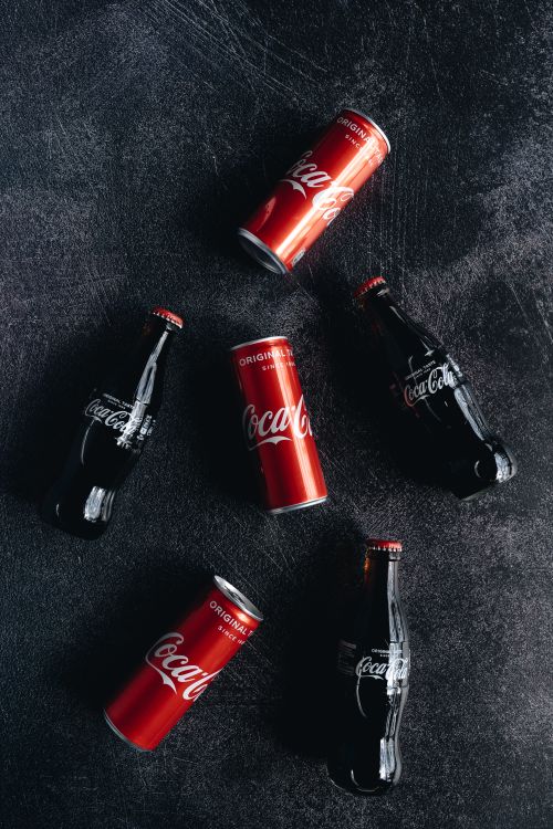 Free Flat lay of Coca Cola cans and bottles on a textured dark surface, highlighting brand contrast. Stock Photo