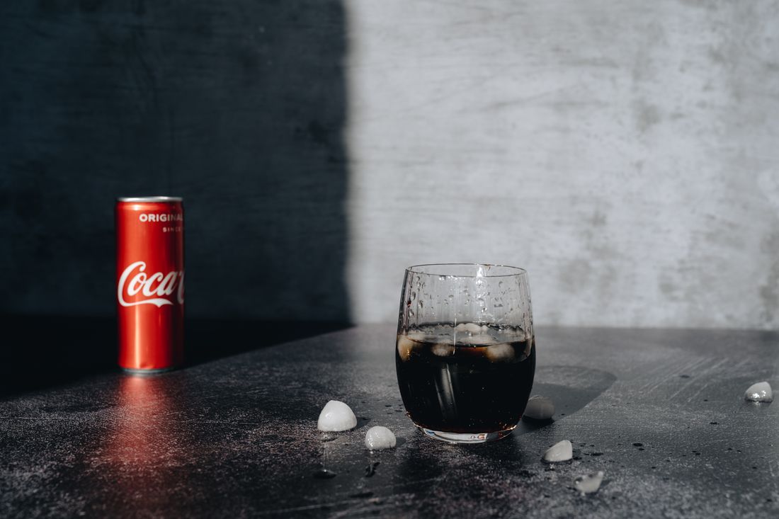 Cola poured from a red can into a glass of ice