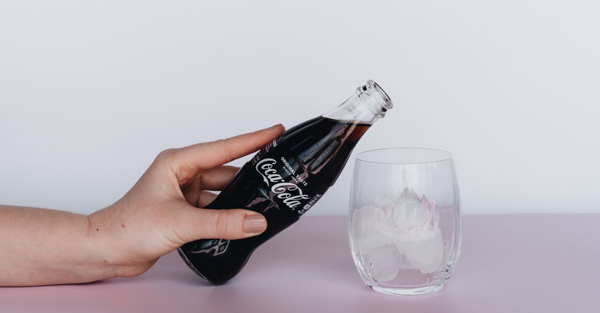 Close-up of a hand pouring heavy cream into a tall glass of dark soda, creating a swirling white cloud effect