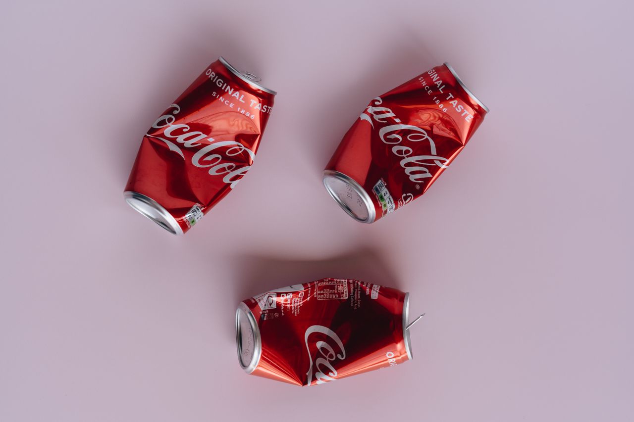 Three crumpled Coca-Cola cans arranged on a pink surface, emphasizing recycling.