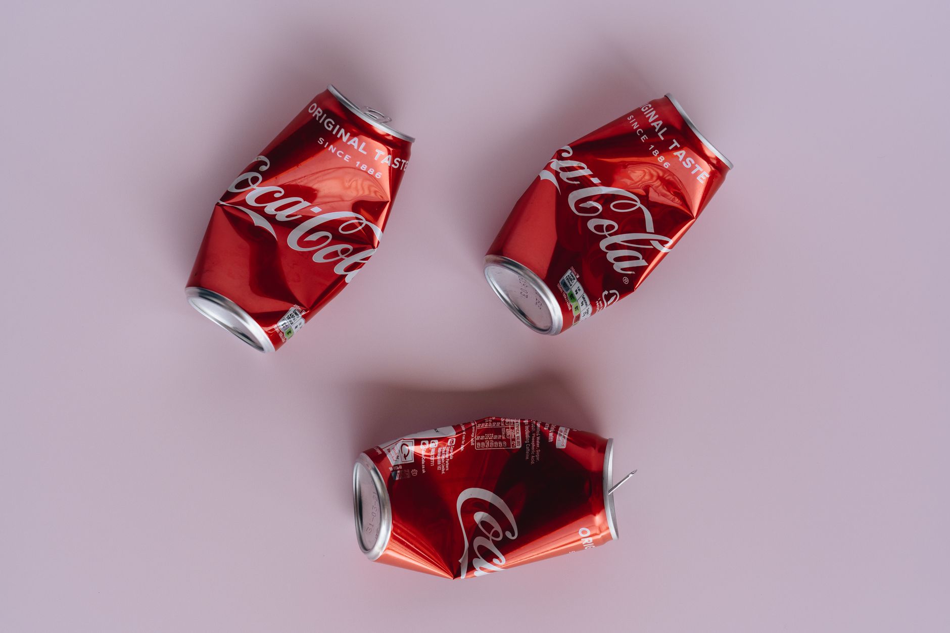Three crumpled Coca-Cola cans arranged on a pink surface, emphasizing recycling.