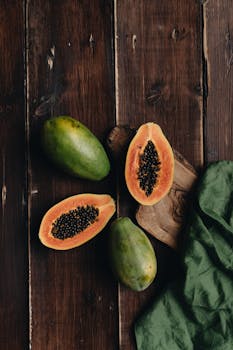 Top view of fresh papaya fruit sliced open on a rustic wooden background.