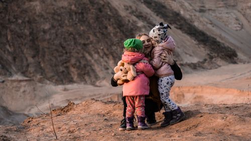 Free Mother and daughters sharing a warm embrace in a scenic outdoor setting, symbolizing family togetherness. Stock Photo