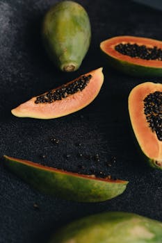 Ripe papaya slices with seeds on a textured dark background, showcasing vibrant colors and freshness.