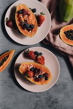 Top view of halves of delicious papaya stuffed with fresh strawberries and ripe raspberries placed on white plate and composed with yummy cut strawberries and blueberries