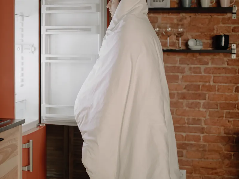 Person wrapped in a blanket checking an open top mount refrigerator in a cozy kitchen Person wrapped in a blanket checking an open top mount refrigerator in a cozy kitchen