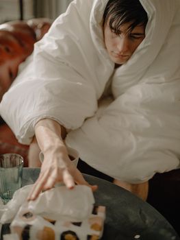 一个裹在毯子里的年轻人伸手去拿纸巾，营造出舒适温馨的氛围