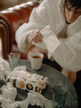 男人裹着毯子坐在纸巾和茶渍中，感觉很不舒服
