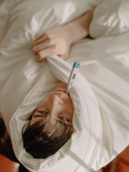 一个年轻人在家裹着毯子，拿着温度计休息