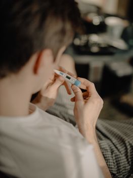 一个年轻人在室内用数字温度计测量体温