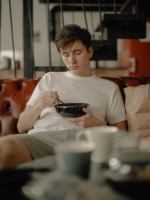Free A relaxed young man eating a meal on a sofa at home, embodying a cozy lifestyle. Stock Photo