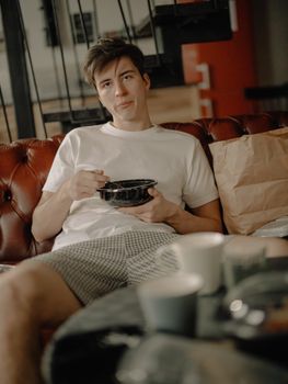 A young man enjoying a meal on a cozy sofa at home, with casual surroundings.
