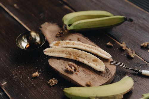 From above composition of peeled cut ripe bananas topped with sweet syrup served on wooden board and decorated with tasty walnuts