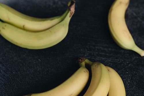 Free From above view of set of bunches of ripe unpeeled yellow bananas placed together on wooden dark shabby surface under bright light Stock Photo