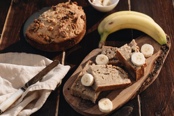 Sliced banana bread on a wooden board with banana rounds, a walnut-topped loaf and bananas