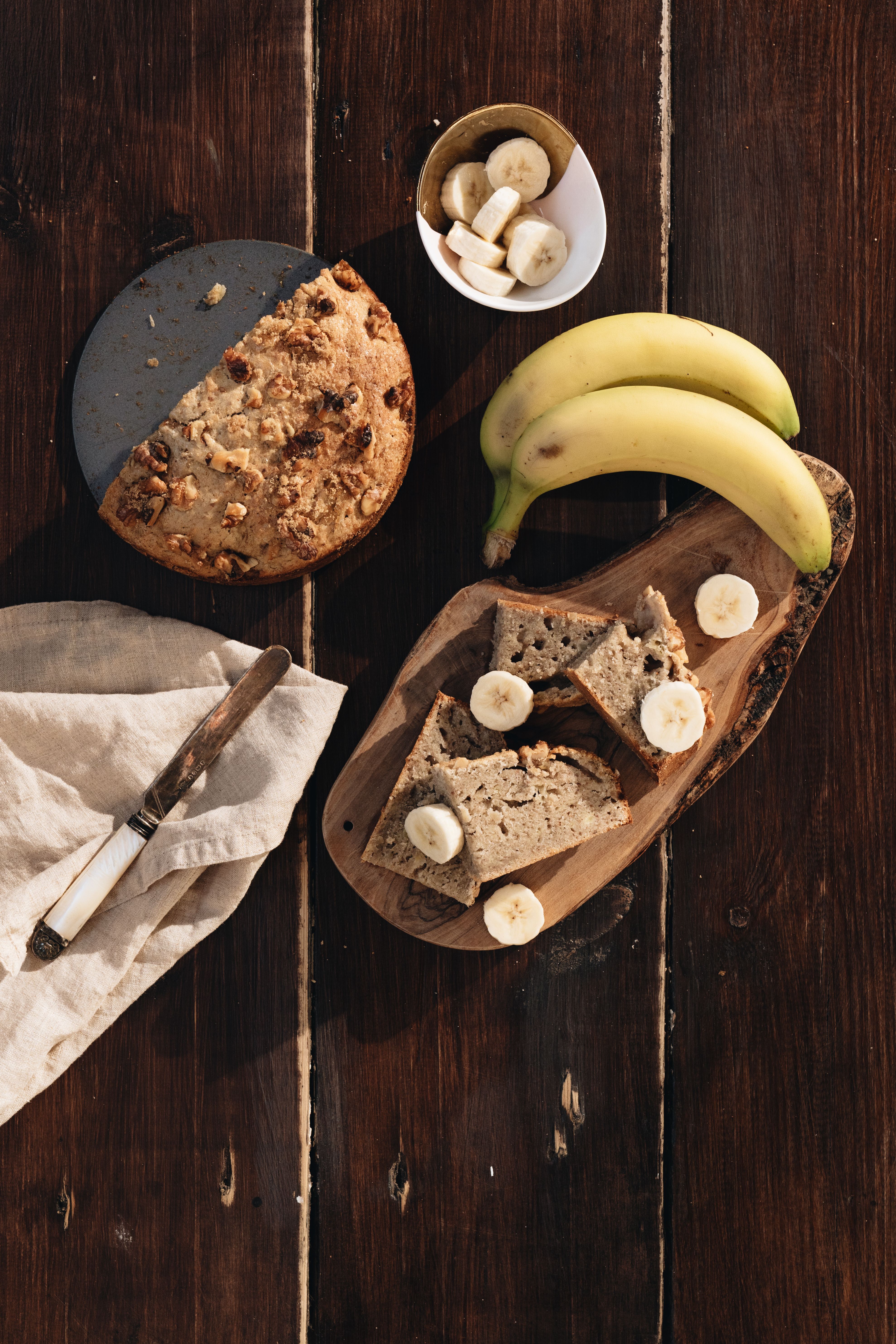 A sliced loaf of banana bread on a wire rack, showing a moist, tight crumb studded with banana flecks.