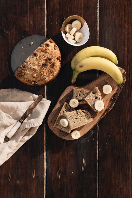 A sliced loaf of banana bread on a wire rack, showing a moist, tight crumb studded with banana flecks.