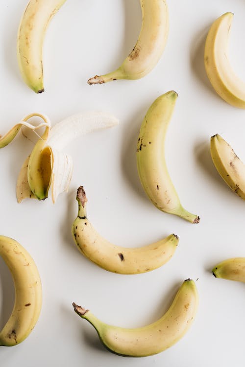 Top view composition of ripe half peeled banana among fresh yellow unpeeled bananas placed on white background under bright light