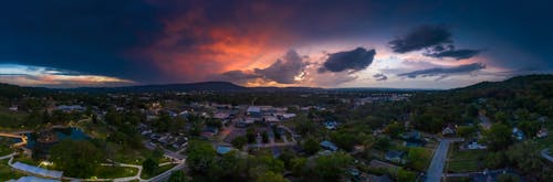 Free Panorama of bright evening sky covered with multi colored clouds above mountain range and town immersed in green Stock Photo
