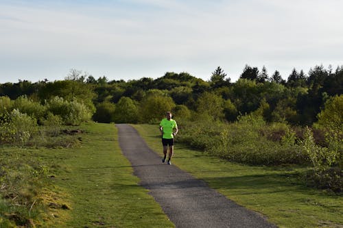 Man in Green Shirt and Black Shorts Running on Pathway