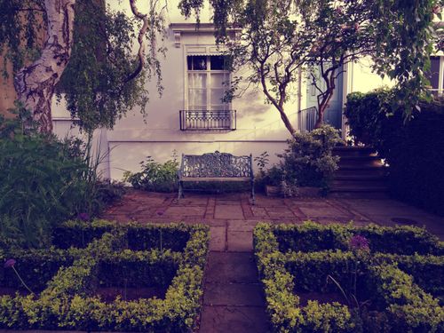 Free A serene outdoor garden with a vintage bench framed by lush greenery and classic architecture. Stock Photo