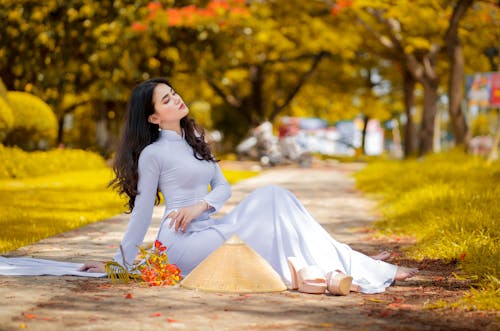 Woman in White Long Sleeve Dress Sitting On Paved Pathway