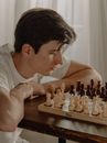 一位年轻男子在舒适的家庭环境中专注于国际象棋对弈，展现出策略与专注
