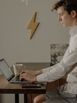 Casual remote work setup with a young man using a laptop in a cozy home environment.