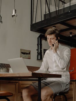 Man working from modern home office using laptop and phone, showcasing remote work lifestyle.