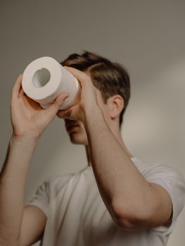白天，一个男人幽默地用厕纸卷在室内充当临时望远镜
